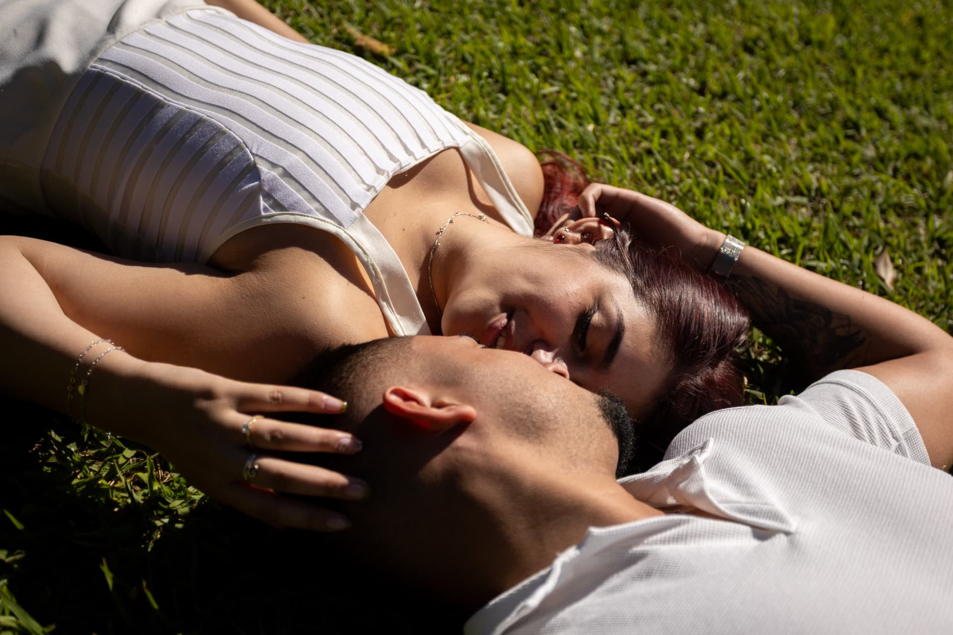 O casal deitado na grama ao sol, rostos próximos e sorrindo