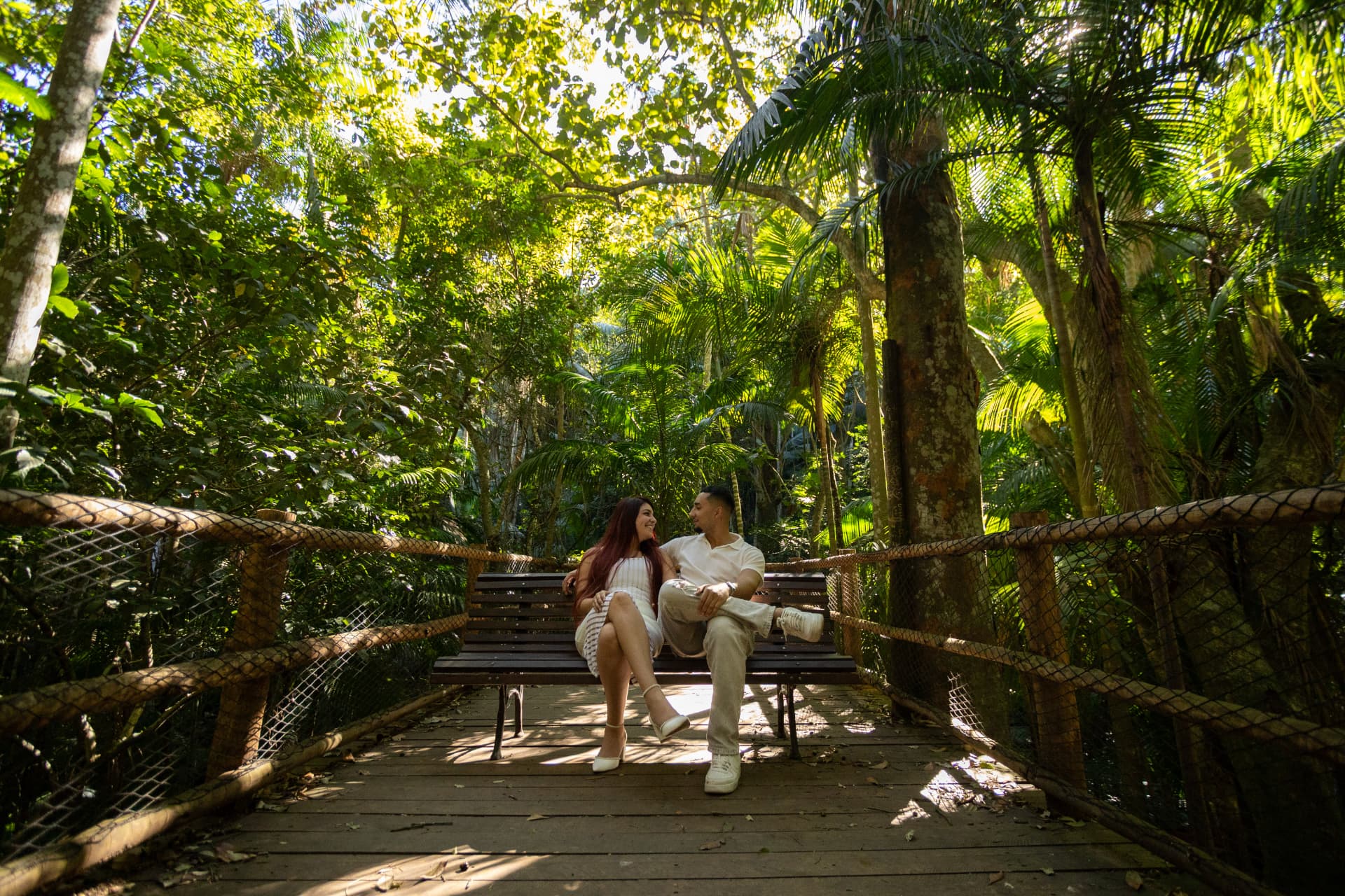 O casal sentado em um banco de madeira em meio à vegetação tropical
