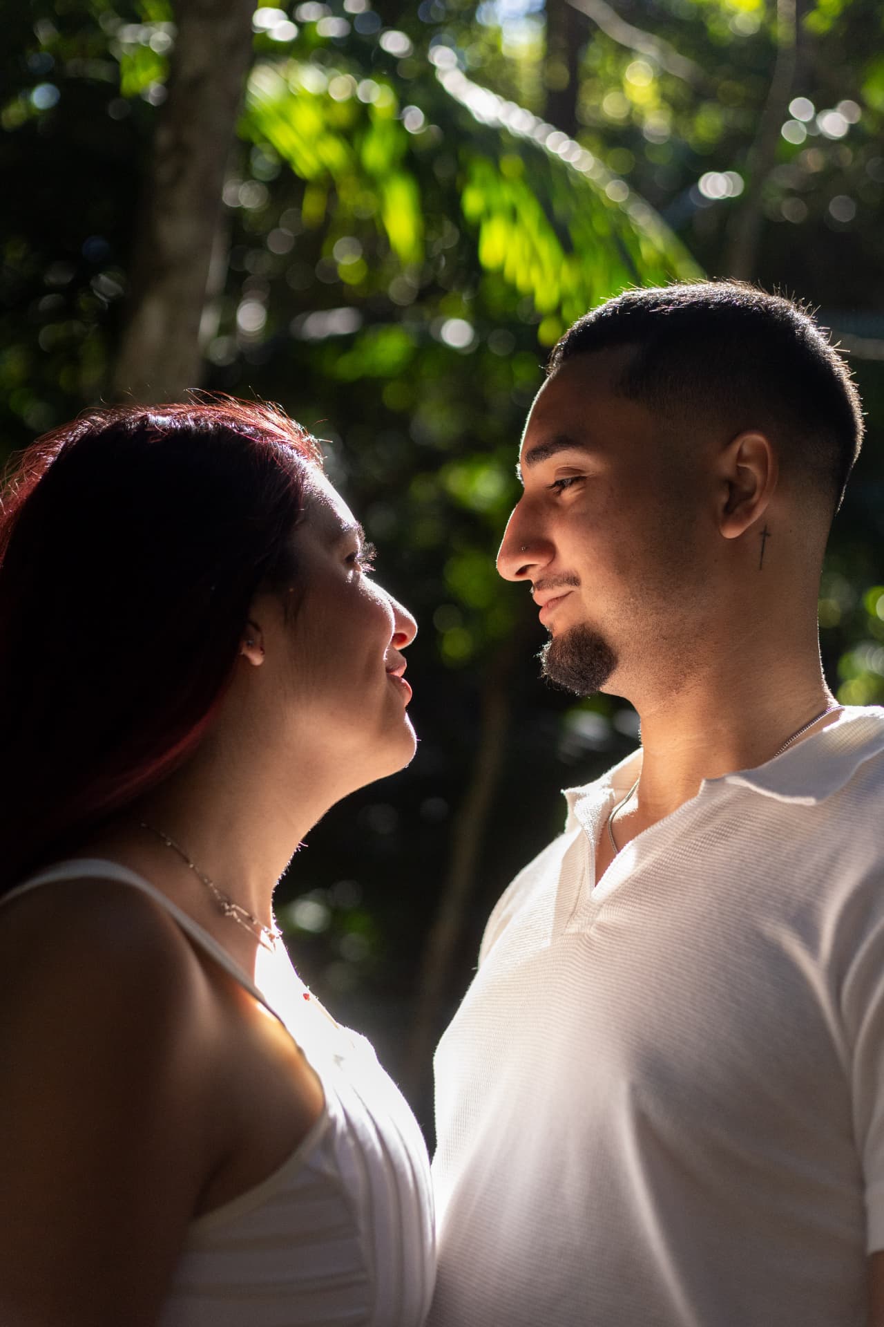 Ketelyn e Carlos frente a frente, sorrindo, com a luz do sol atravessando a mata